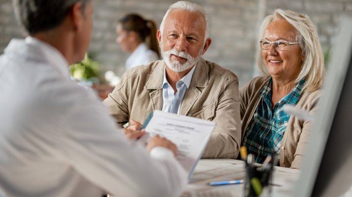 Happy senior couple going through medical insurance paperwork with a doctor.