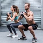 Kneeling muscular couple exercising with kettlebells