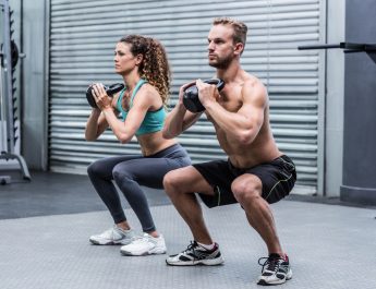 Kneeling muscular couple exercising with kettlebells