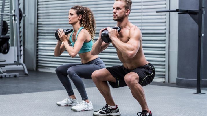 Kneeling muscular couple exercising with kettlebells